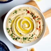 A bowl of hummus without garlic drizzled with olive oil and garnished with paprika and chopped parsley.