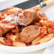 A close up photo of a bowl of penne pasta with pieces of cut up Italian sausage. There is parmesan cheese grated over top.