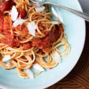 A bowl of pasta with a fork and spoon in the bowl with cheese shavings sprinkled over top.