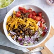 Finished cheeseburger bowl with lettuce, beef, onions, cheese, tomatoes and drizzled with burger sauce.