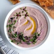 A bowl with red kidney bean hummus garnished with olive oil, pepitas and micro greens.