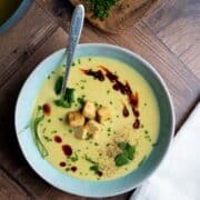 A bowl of leek, potato and cauliflower soup in a bowl, garnished with croutons, chives, cilantro and chili oil.