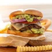 A Tex Mex hamburger with cheese, guacamole, tomato and red onion.