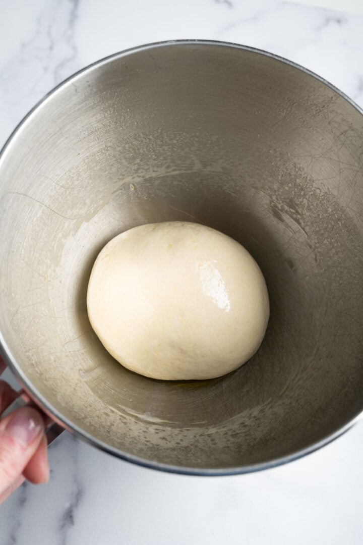 Oiled, shaped pizza dough ball in the bowl of a stand mixer.