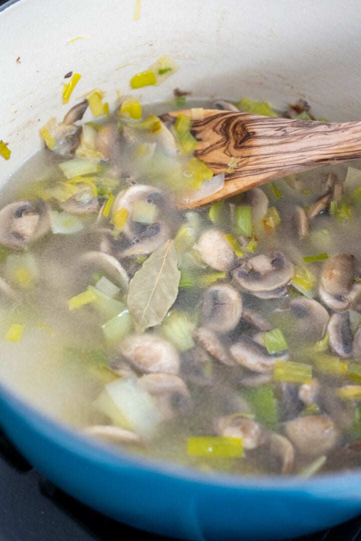 A Dutch oven with mushrooms, leeks, water, bay leaf.