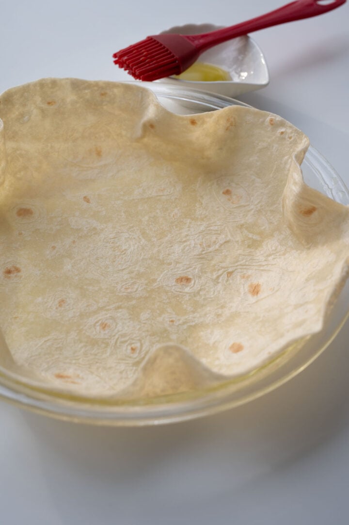 A uncooked tortilla in an oiled pie plate.