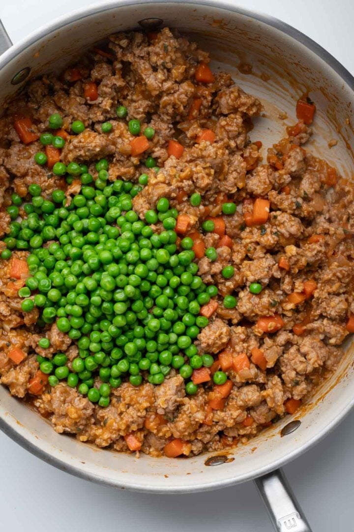 A skillet with cooked ground pork with fresh peas.