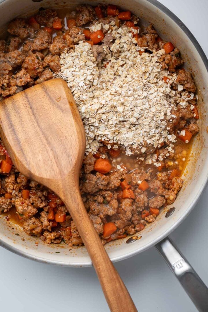 Adding the oats to the skillet with the cooked pork and vegetables.