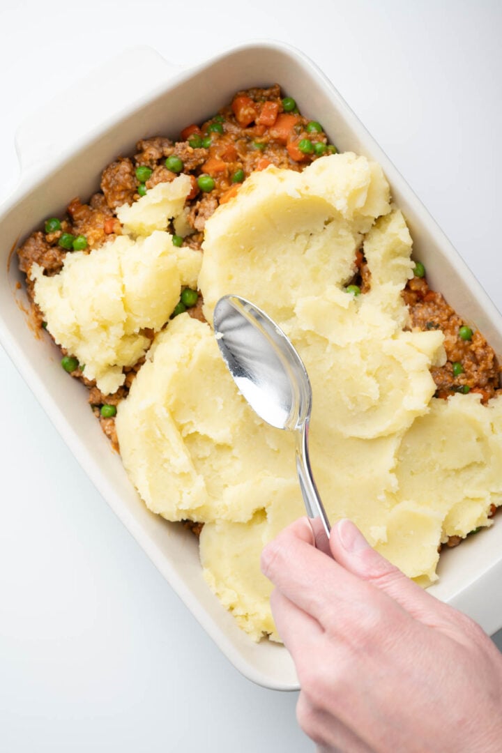 Spreading the mashed potatoes over the cooked pork filling.