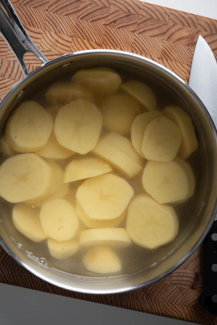 Sliced potatoes in a saucepan filled with water.