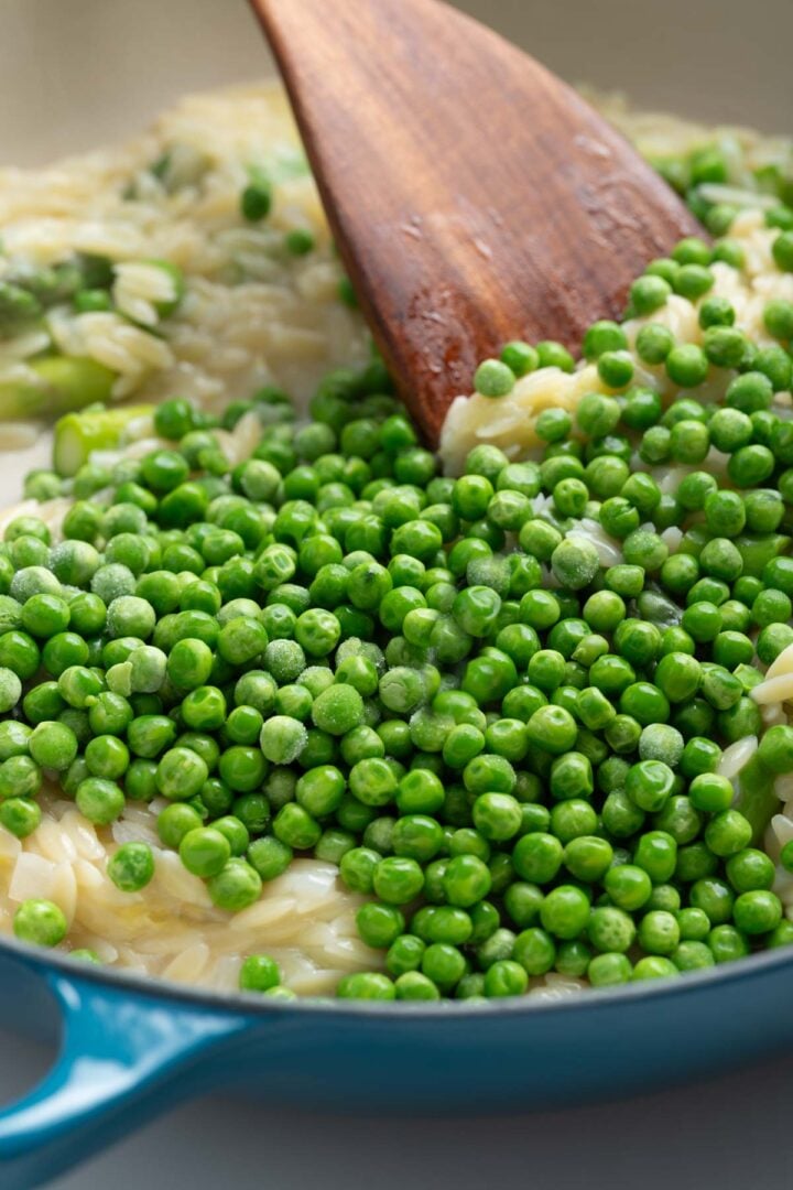 Stiring peas into a skillet with orzo and asparagus.