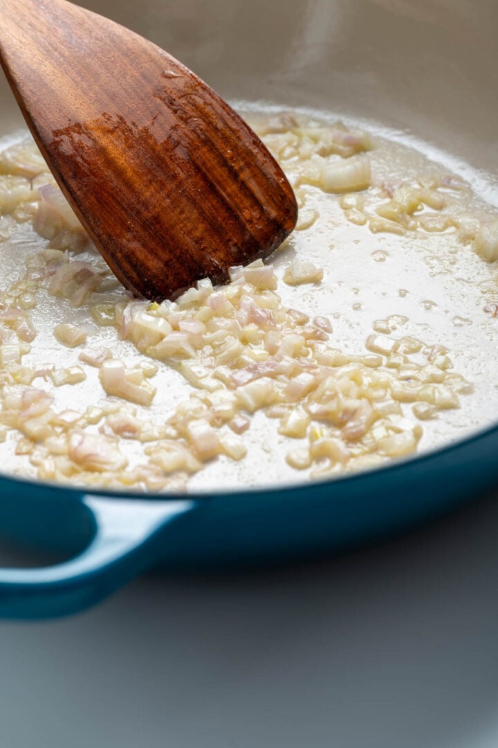 Frying shallots in a skillet with a wooden spoon.